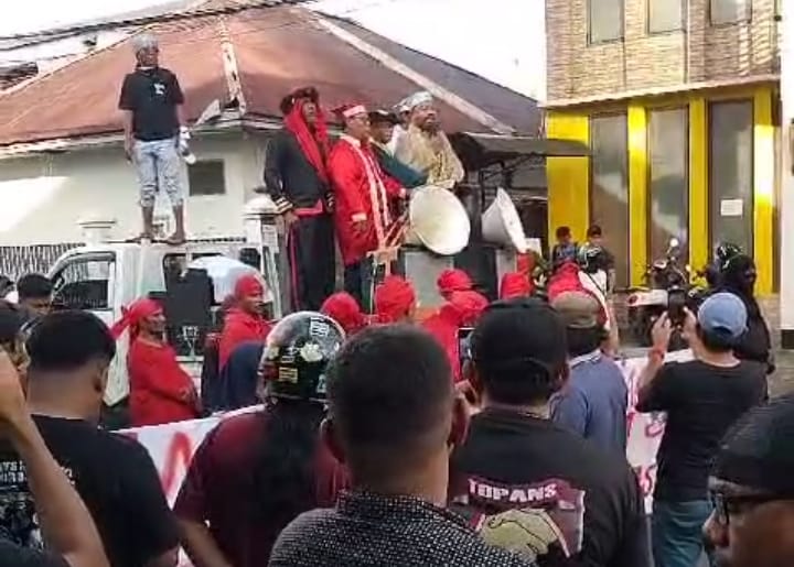 Foto: Zulkifli Marsaoly mengenakan pakaian sadaria warna crame disertai tuala talam saat menggelar aksi demonstrasi di depan Kantor KPU Maluku Utara. (Istimewa)